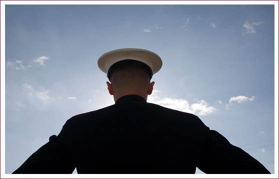 Group 8-3 A person in a uniform with a white cap stands facing the sky, silhouetted against a bright sun and scattered clouds.